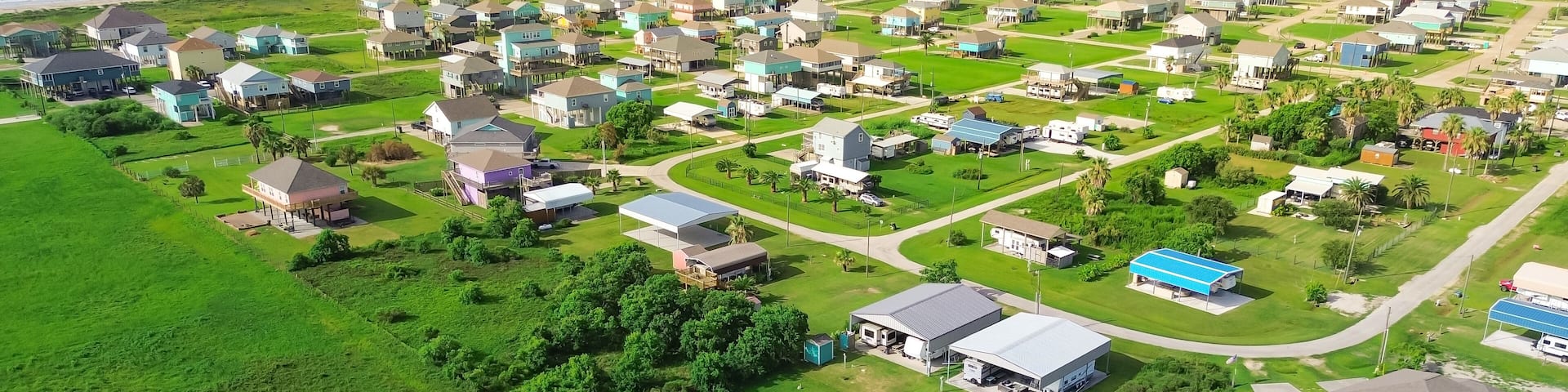Large vacant land near raised beach house with spacious grassy backyard in Port Bolivar, Texas. Elevated sturdy stilts homes, design common along Gulf Coast for storm resilience, flood protection