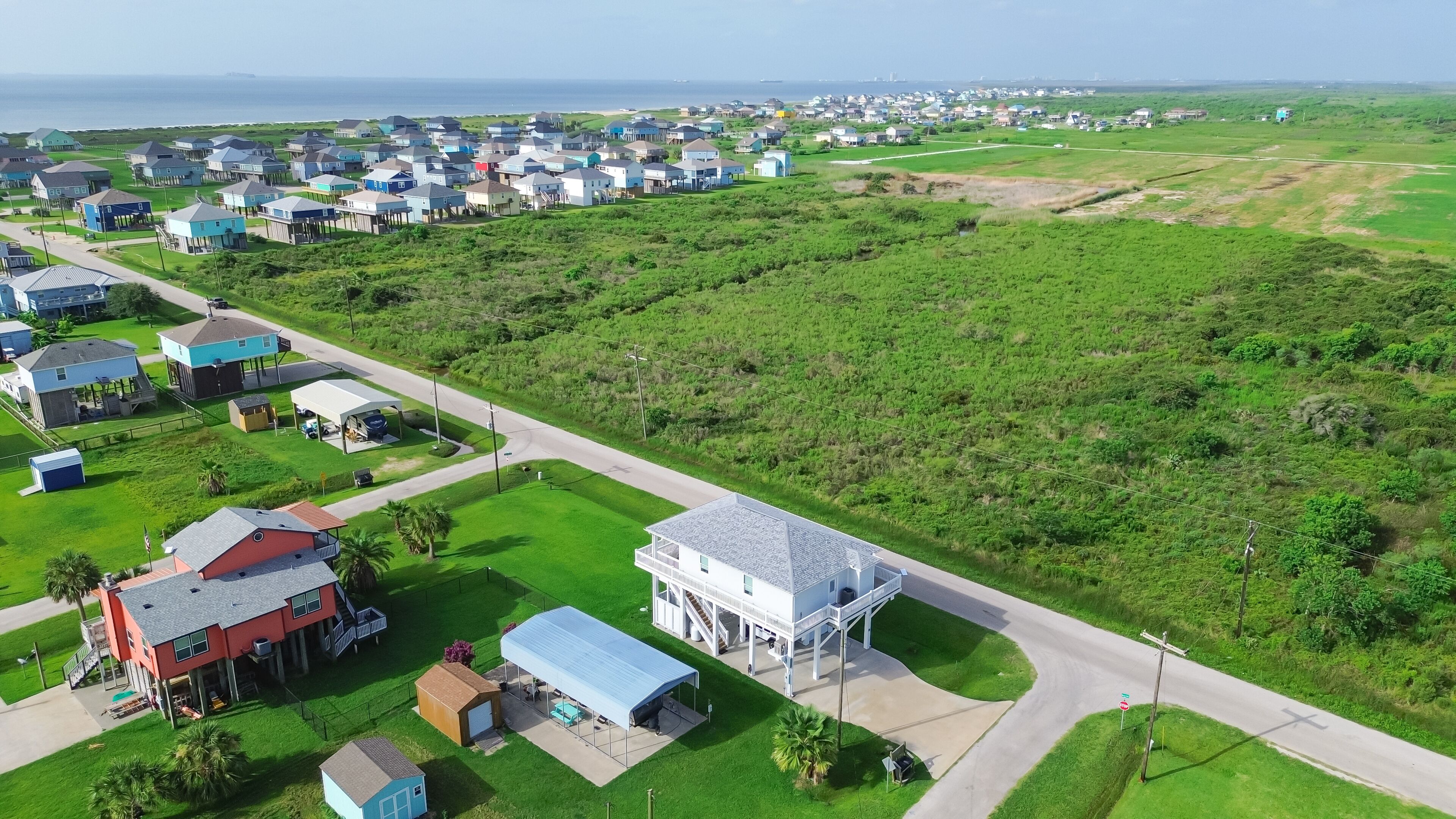 Large vacant land near raised beach house with spacious grassy backyard in Port Bolivar, Texas. Elevated sturdy stilts homes, design common along Gulf Coast for storm resilience, flood protection