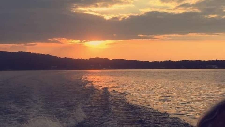 A sunset over a body of water with a boat creating waves.