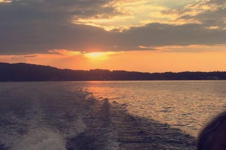 A sunset over a body of water with a boat creating waves.