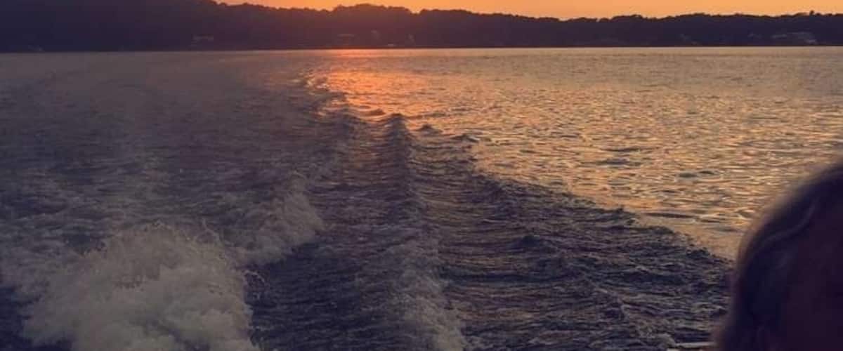 A sunset over a body of water with a boat creating waves.