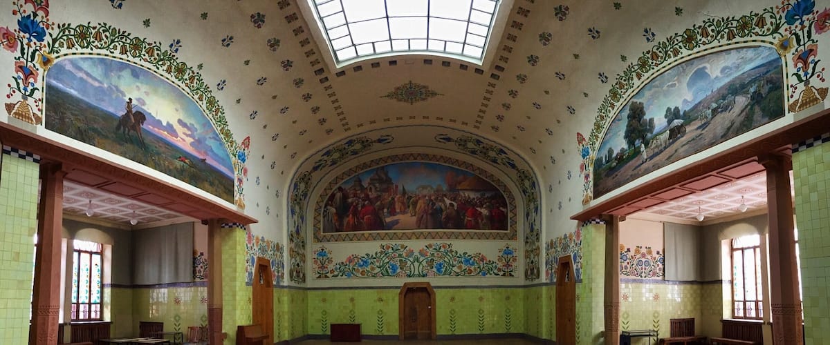 A spacious hall with ornate murals, a high ceiling, and patterned walls.