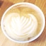 Een kop koffie met een blader-achtig latte art patroon op een houten ondergrond.