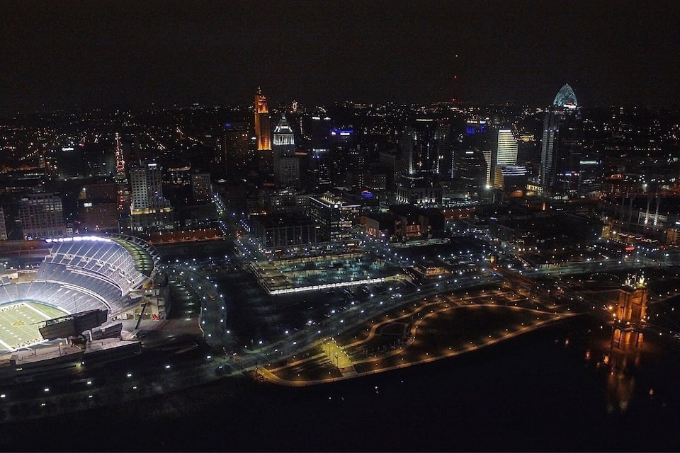 Un paisaje urbano nocturno con un estadio grande, edificios iluminados y un río.
