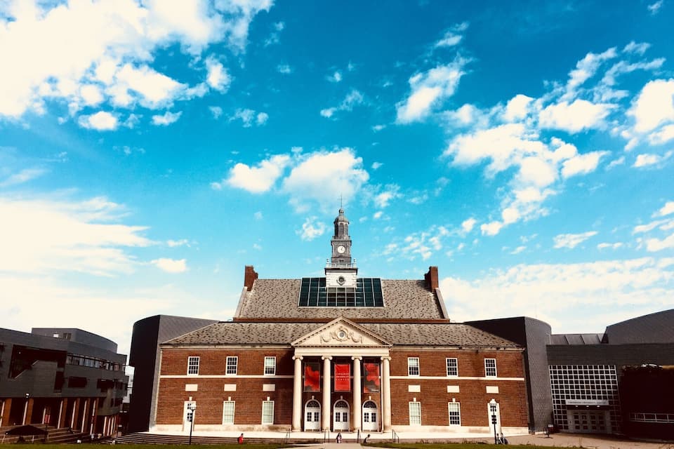 A large brick building with a clock tower, columns, and a red banner.