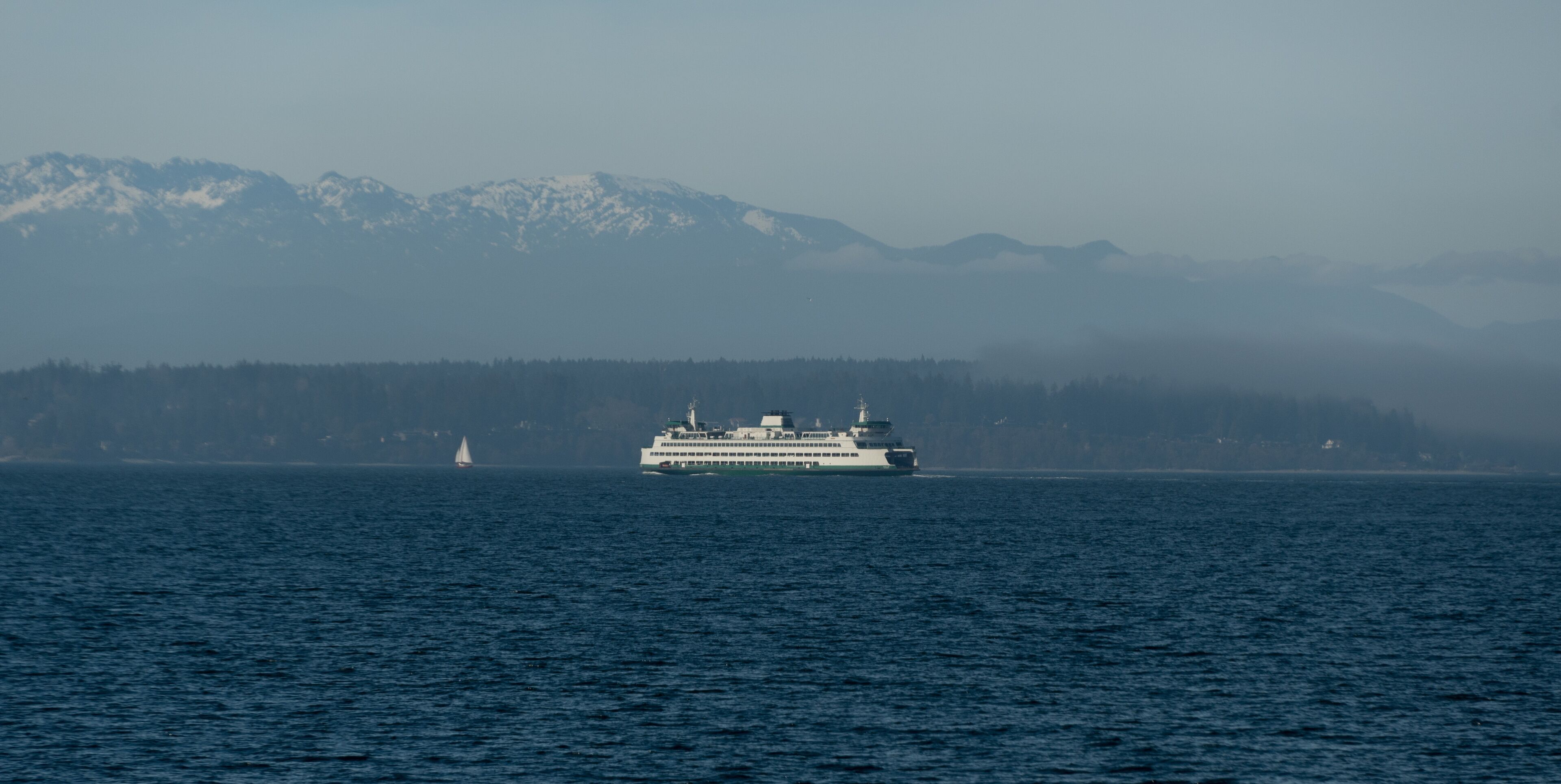 Ferry passing Bainbridge island  covered by low fog with small sailboat  in front of it
