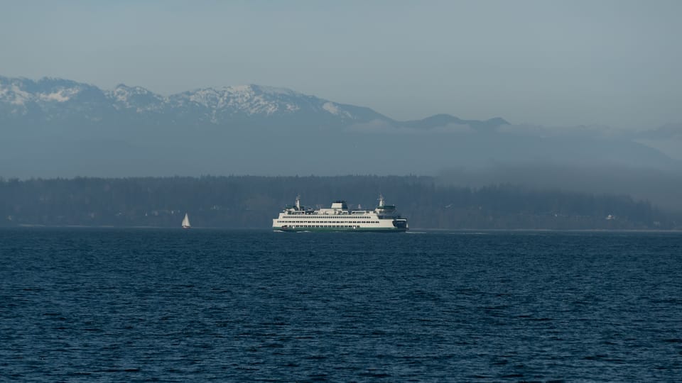 Ferry passing Bainbridge island covered by low fog with small sailboat in front of it