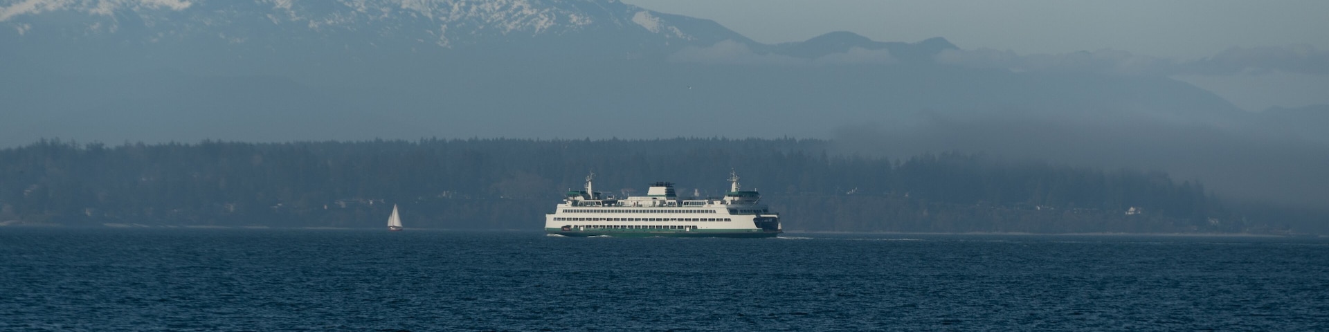 Ferry passing Bainbridge island covered by low fog with small sailboat in front of it