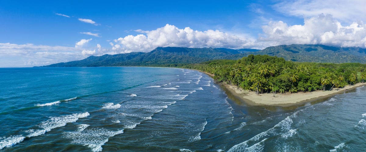 A tropical beach with clear blue waters, a sandy shore, and lush green vegetation.