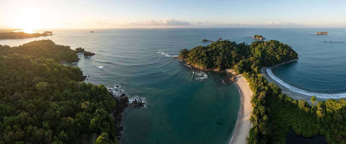 Vista aérea de una isla tropical con playa, exuberante bosque y aguas azules cristalinas.
