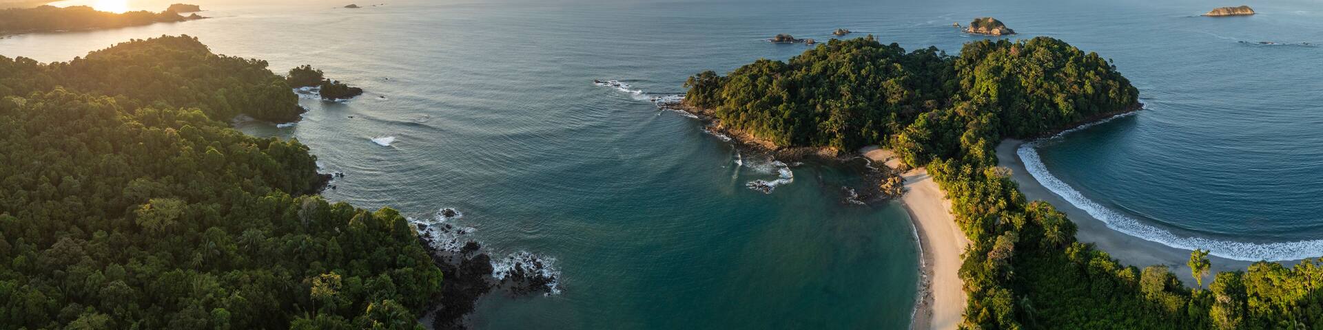 Vue aérienne d’une île tropicale avec une plage, une forêt dense et des eaux d’un bleu limpide.