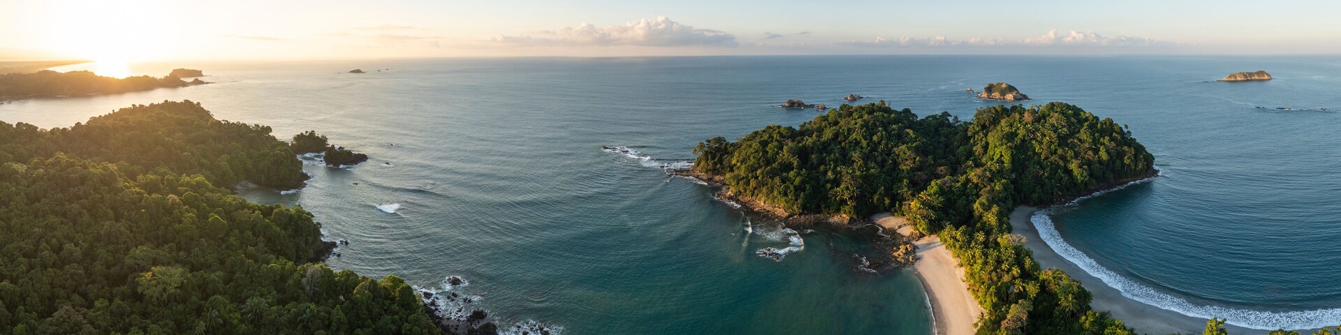 Vista aérea de uma ilha tropical com praia, floresta densa e águas azul-claras.
