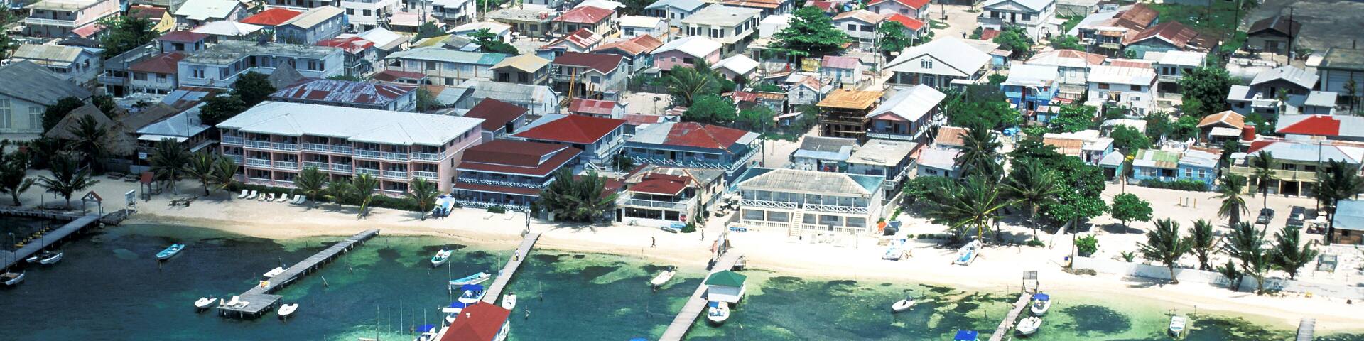 An aerial view of a coastal town with clear turquoise waters, a pier, and numerous buildings.