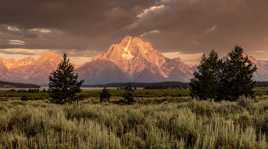 A mountain range with a lake in the foreground and a cloudy sky.