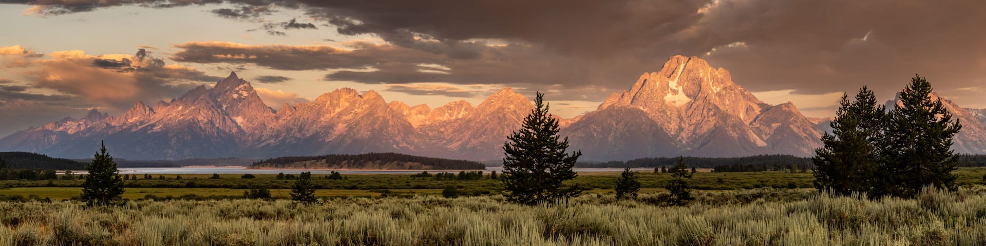 A mountain range with a lake in the foreground and a cloudy sky.
