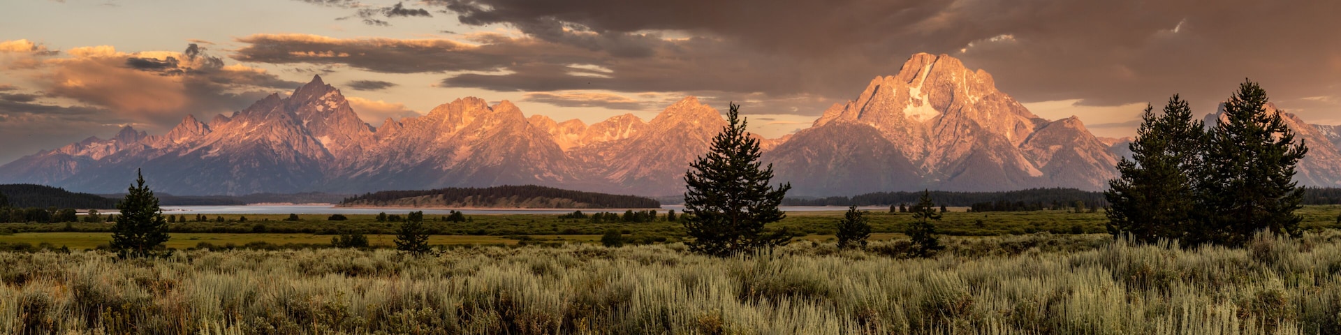 A mountain range with a lake in the foreground and a cloudy sky.