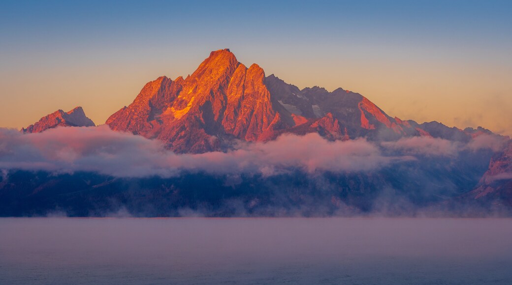 A mountain peak with a golden glow, surrounded by clouds and mist.