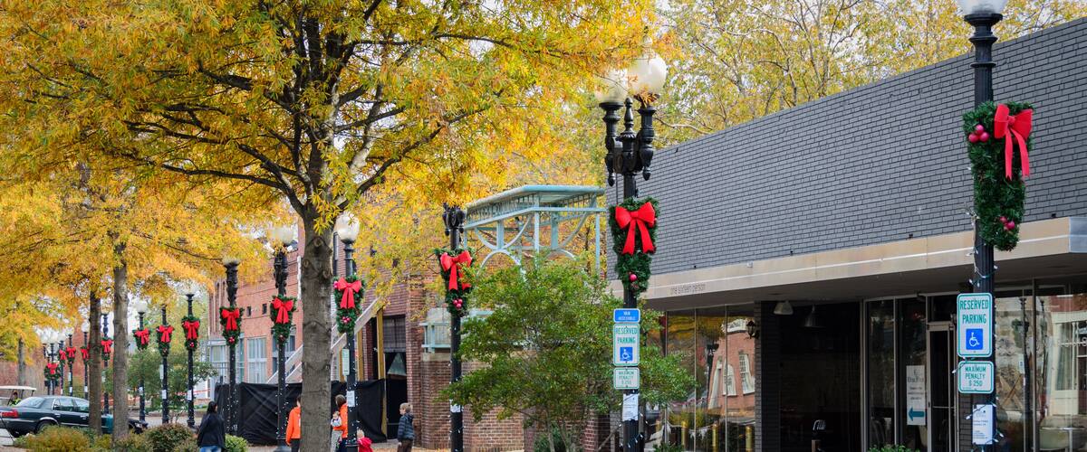 A street lined with trees decorated with red bows and garlands, a brick building with a glass entrance, and a reserved parking sign.
