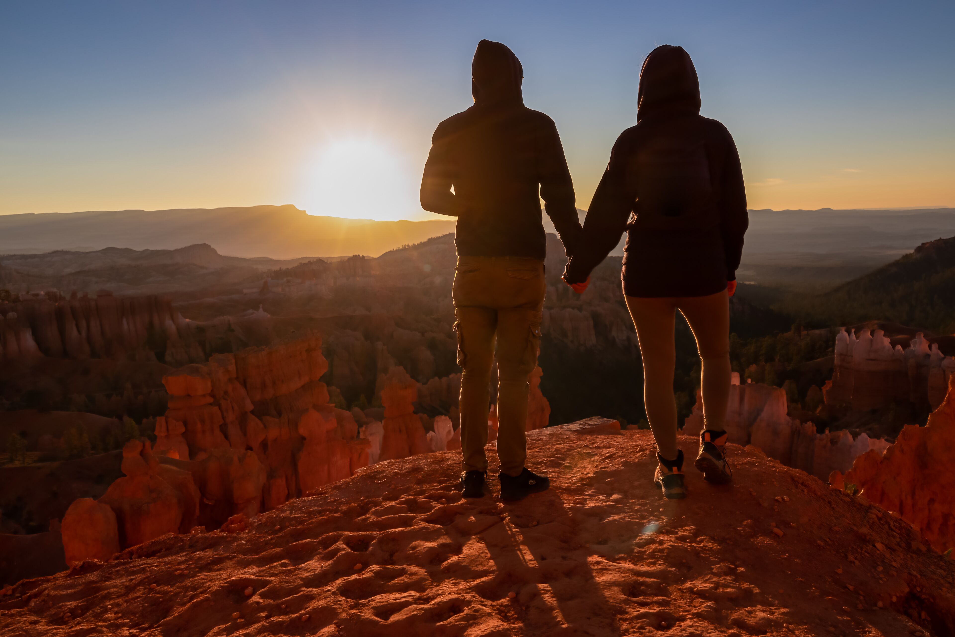 Loving happy couple with panoramic morning sunrise view on sandstone rock formation of Thor hammer in Bryce Canyon National Park, Utah, USA. Golden hour colored hoodoos in unique natural amphitheatre