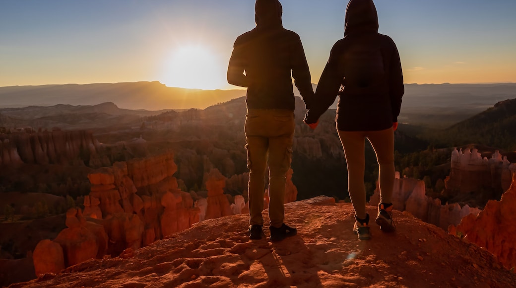 Loving happy couple with panoramic morning sunrise view on sandstone rock formation of Thor hammer in Bryce Canyon National Park, Utah, USA. Golden hour colored hoodoos in unique natural amphitheatre