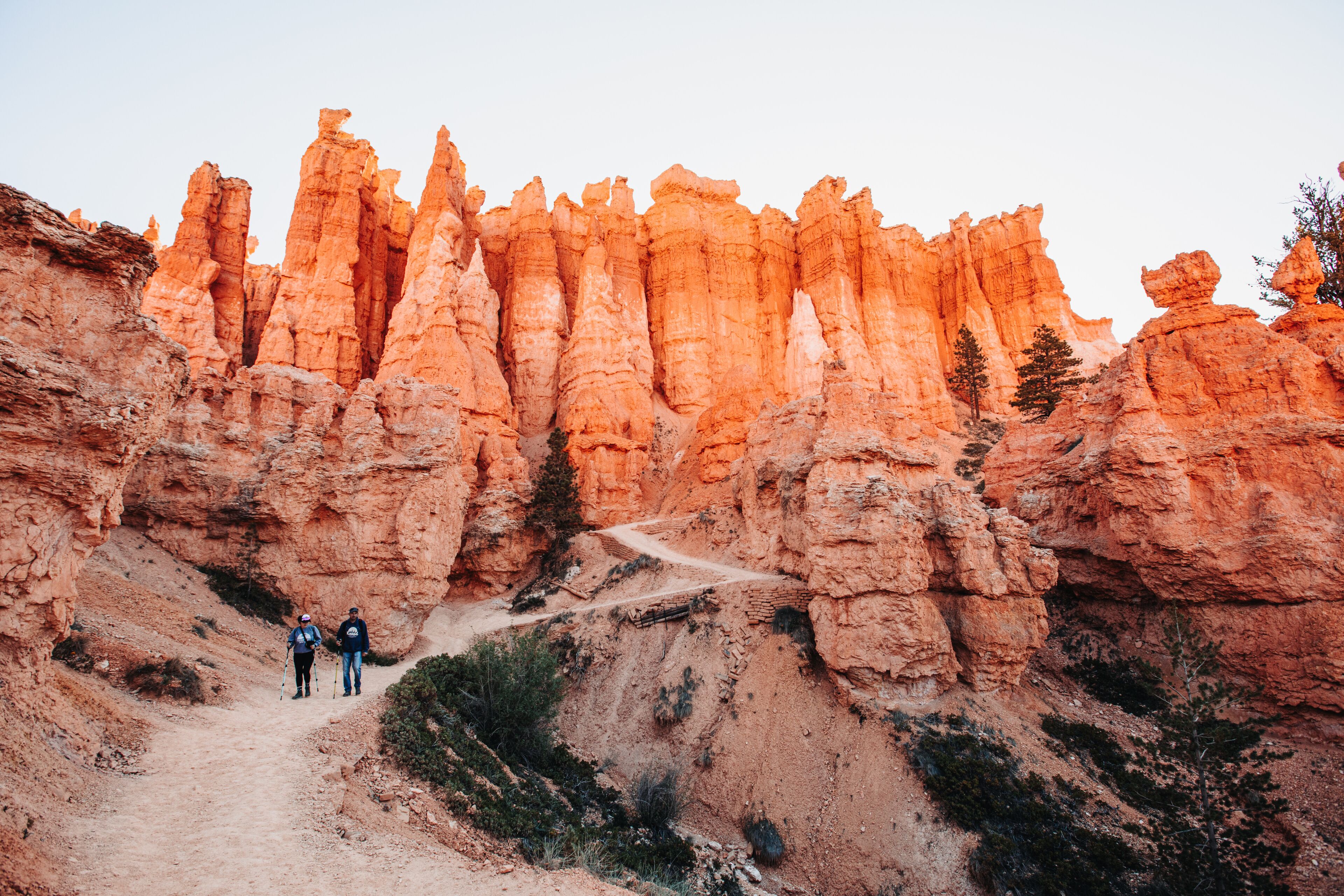 Hikers on a canyon trail with tall, orange rock spires towering