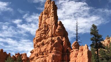 A prominent red rock formation with a clear sky and scattered clouds.