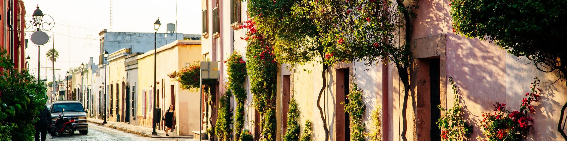 A cobblestone street lined with buildings, some with balconies and flowering plants.