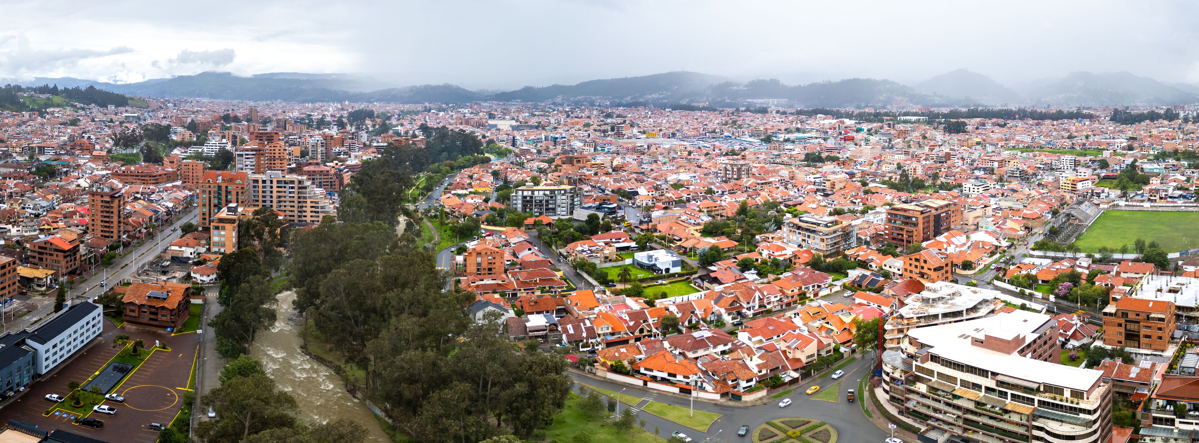 A breathtaking panoramic drone view of Cuenca, Ecuador, showcasing the city's vibrant architecture, lush green spaces, and the Tomebamba River winding through its heart.