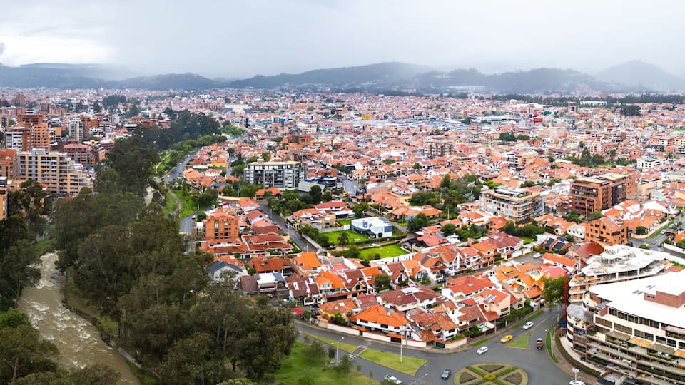 A breathtaking panoramic drone view of Cuenca, Ecuador, showcasing the city's vibrant architecture, lush green spaces, and the Tomebamba River winding through its heart.