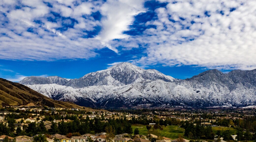 Aerial panorama of snow covered San Gorgonio and Little San Bernardino Mountains on a winter day above Yucaipa Valley with blue sky, white clouds, houses, hills