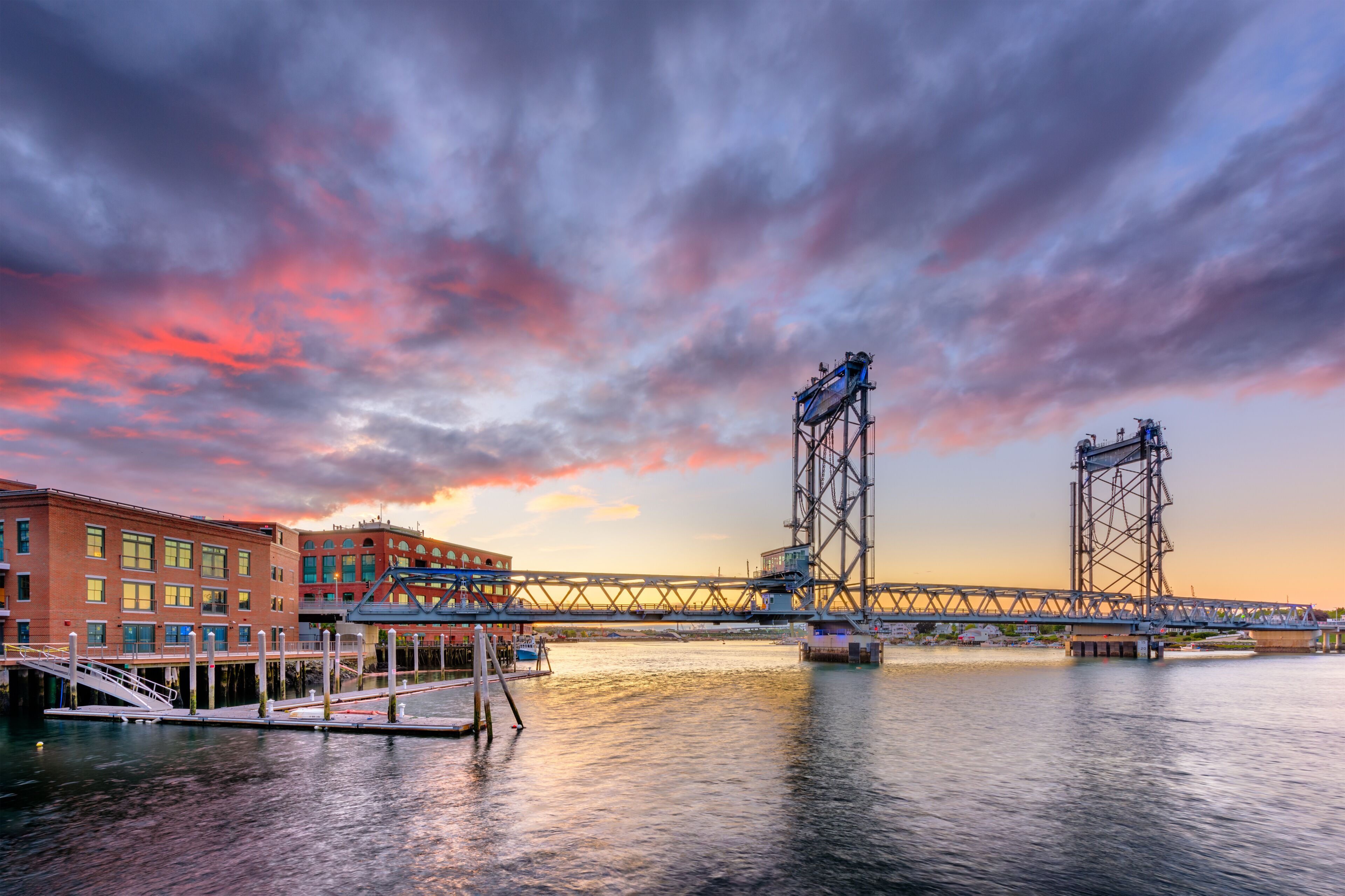 A bridge with a lift mechanism over a body of water, a dock, and buildings along the waterfront.