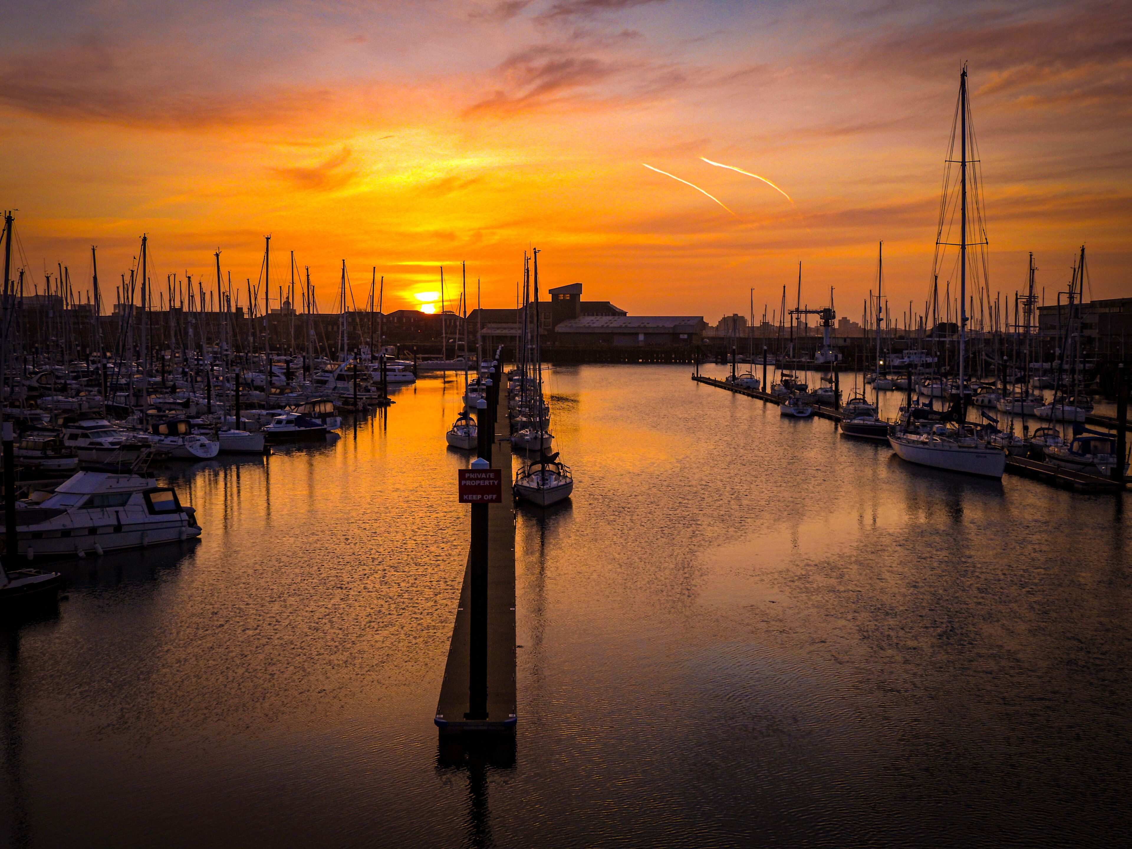 A marina at sunset with numerous sailboats docked.