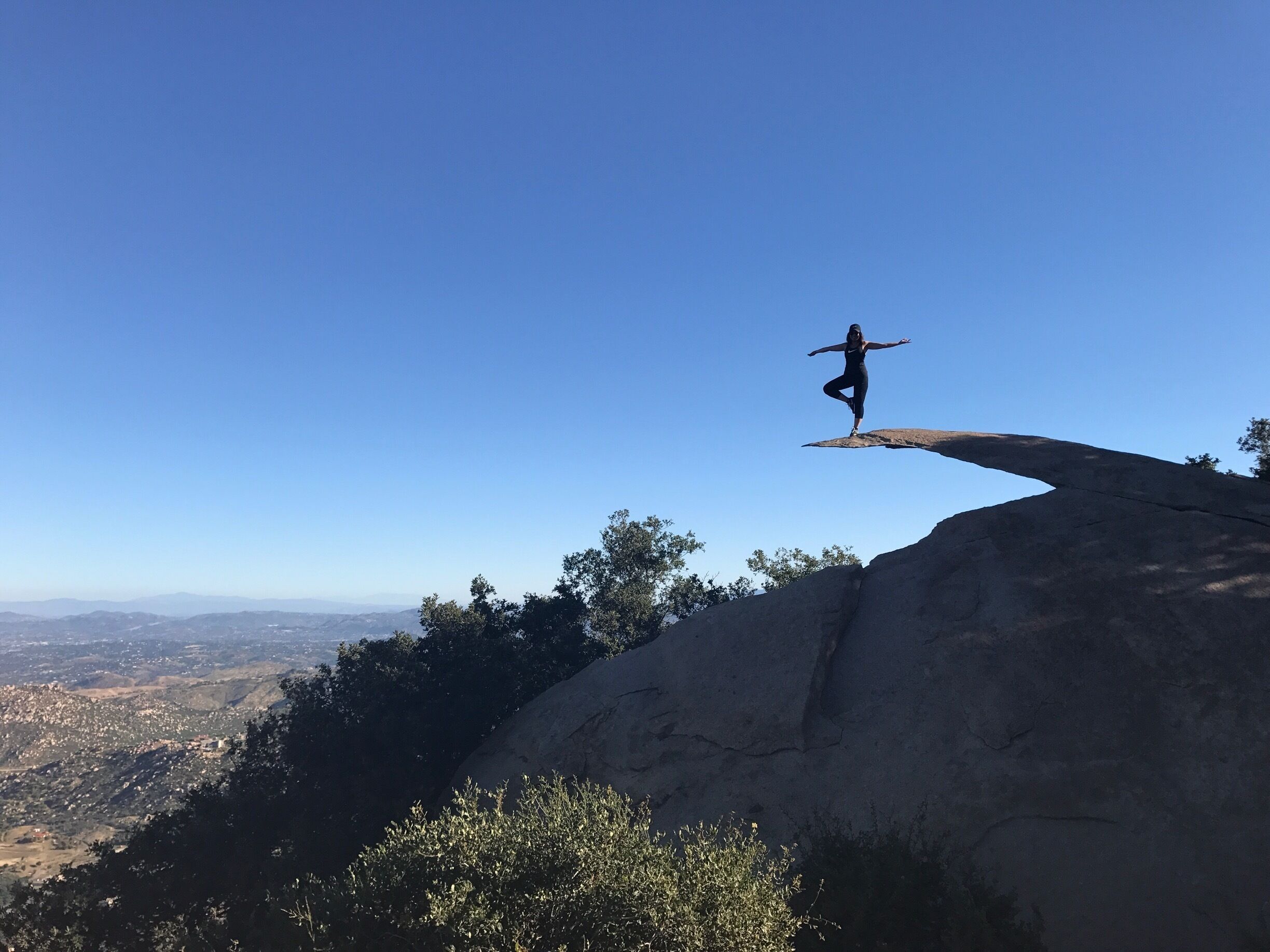 A person performing a balancing act on a rock formation with a clear view of the surrounding landscape.