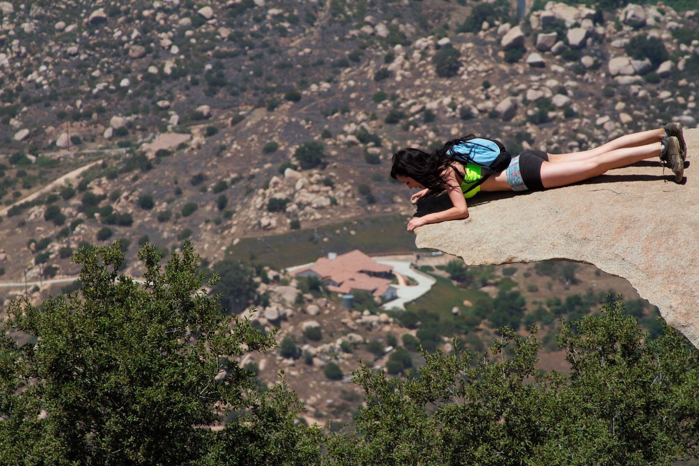 A person lying on a rock ledge overlooking a valley with scattered houses.