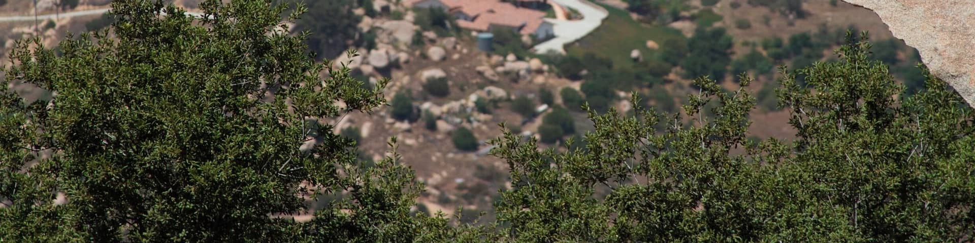 A person lying on a rock ledge overlooking a valley with scattered houses.