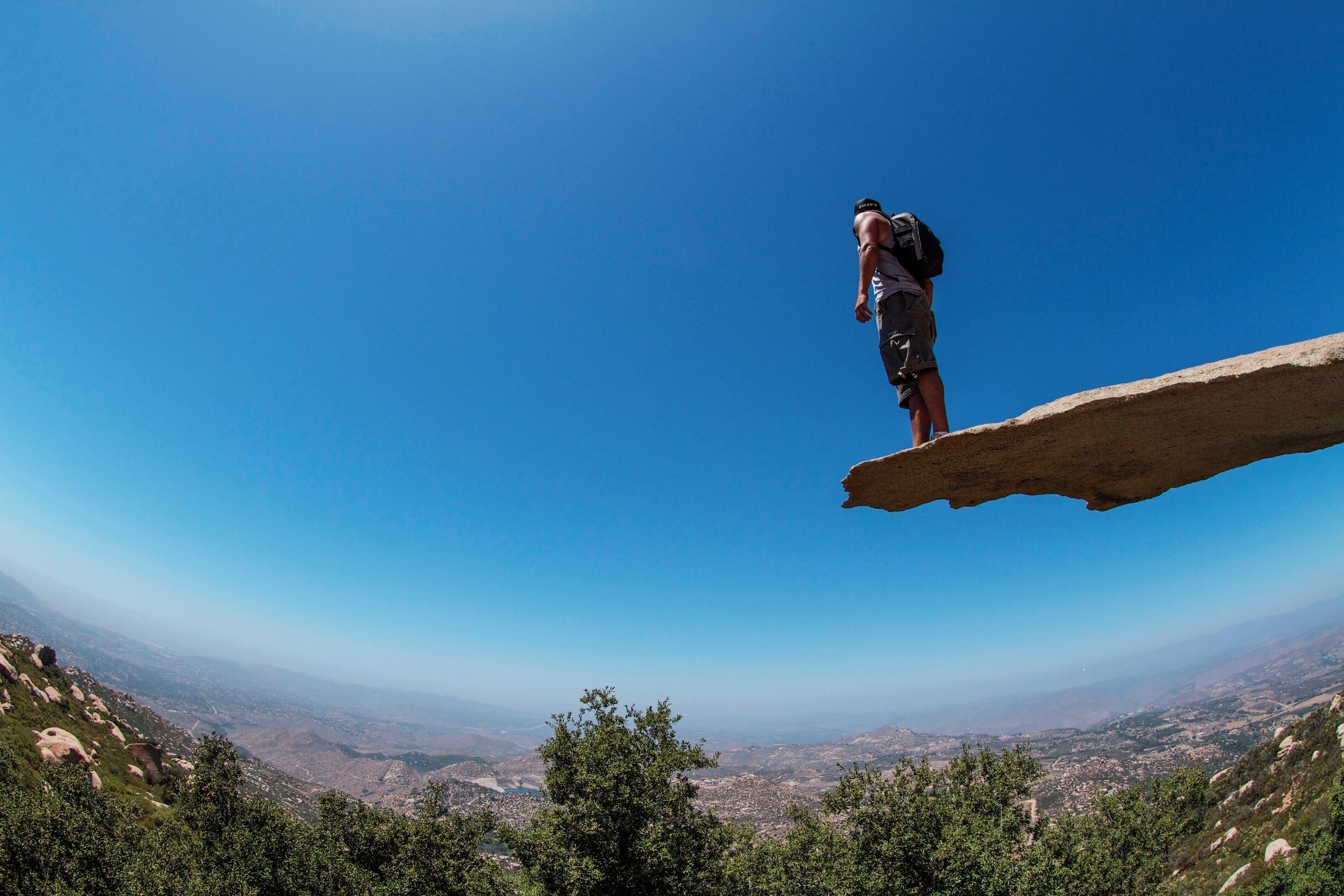 A person standing on a rock ledge overlooking a valley.