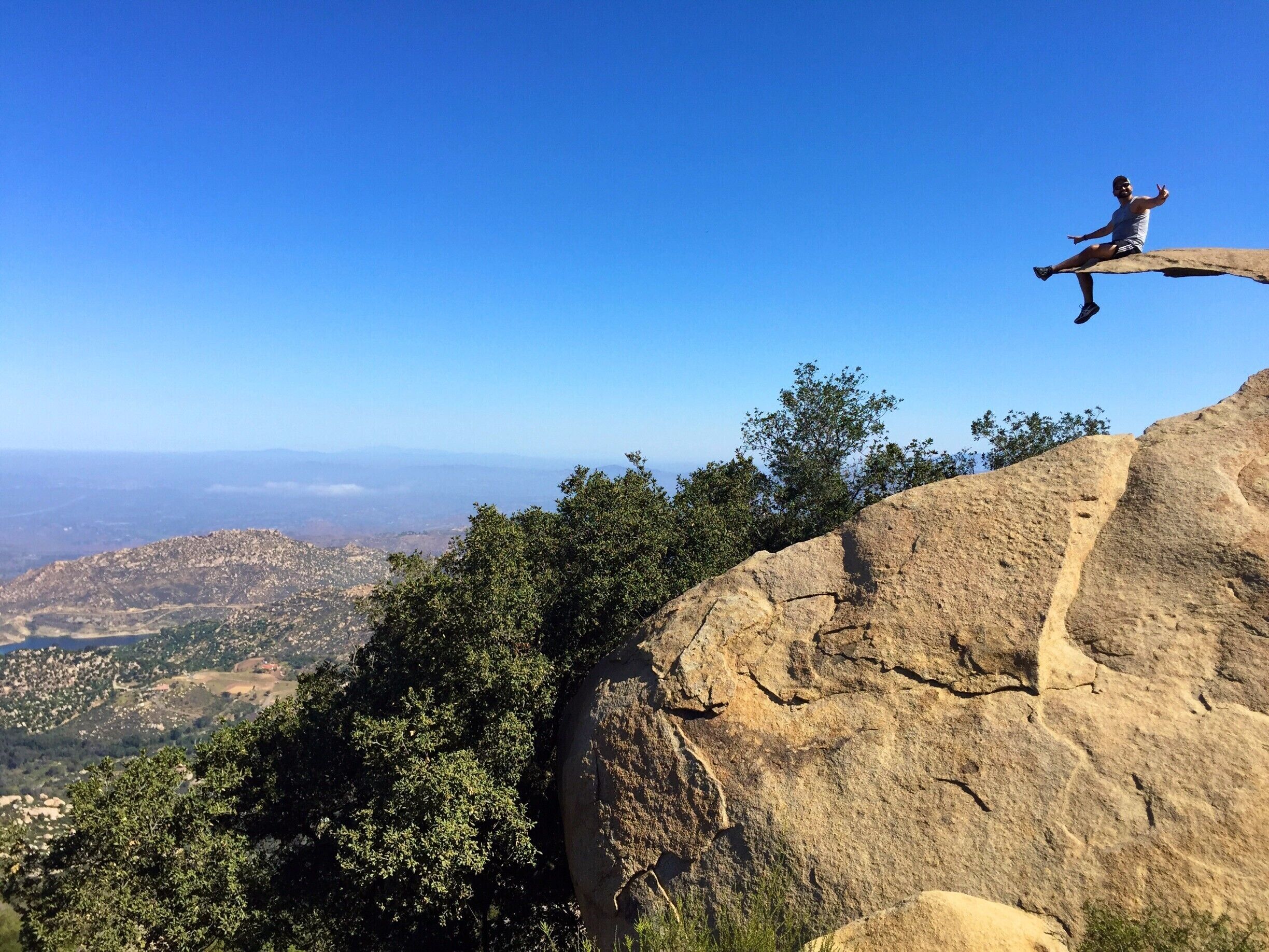 A person sitting on a rock ledge with a view of a valley below.