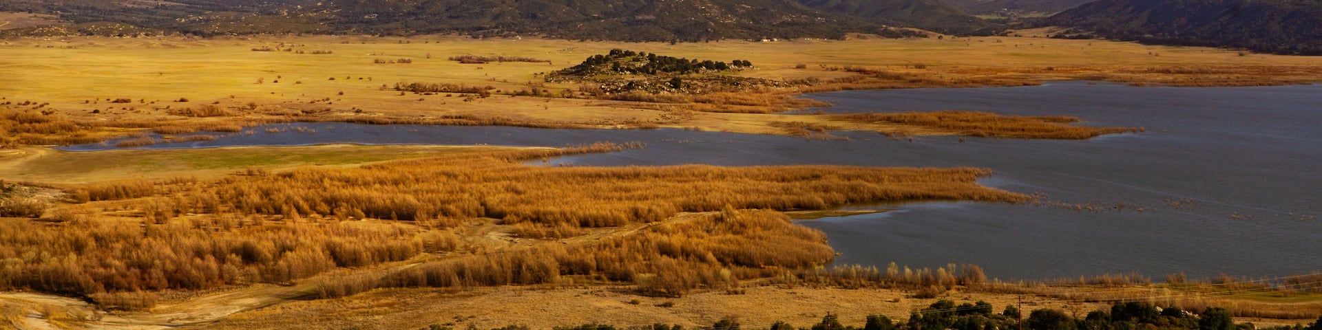 A vast landscape with a large body of water, surrounded by dry grasslands and distant mountains.