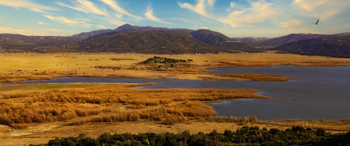A vast landscape with a large body of water, surrounded by dry grasslands and distant mountains.