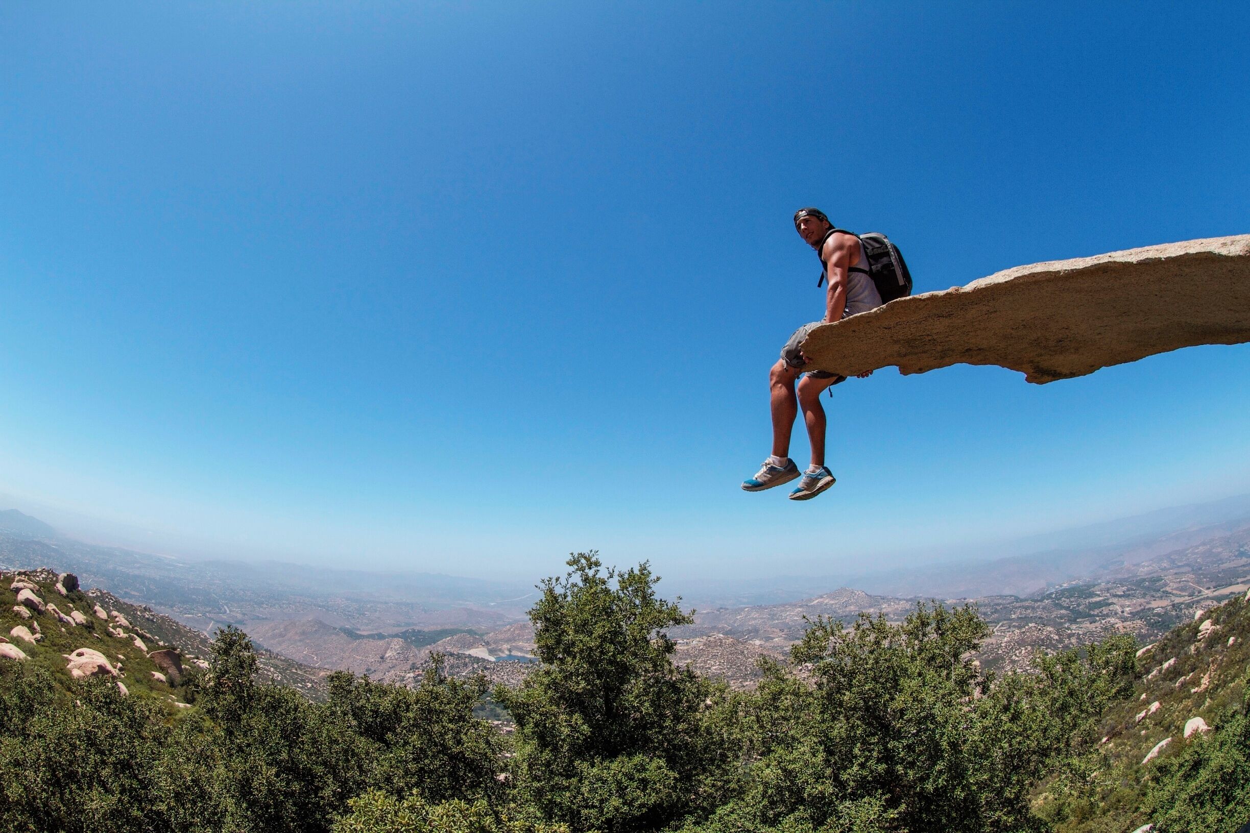 A person sitting on a rock ledge overlooking a mountainous landscape.