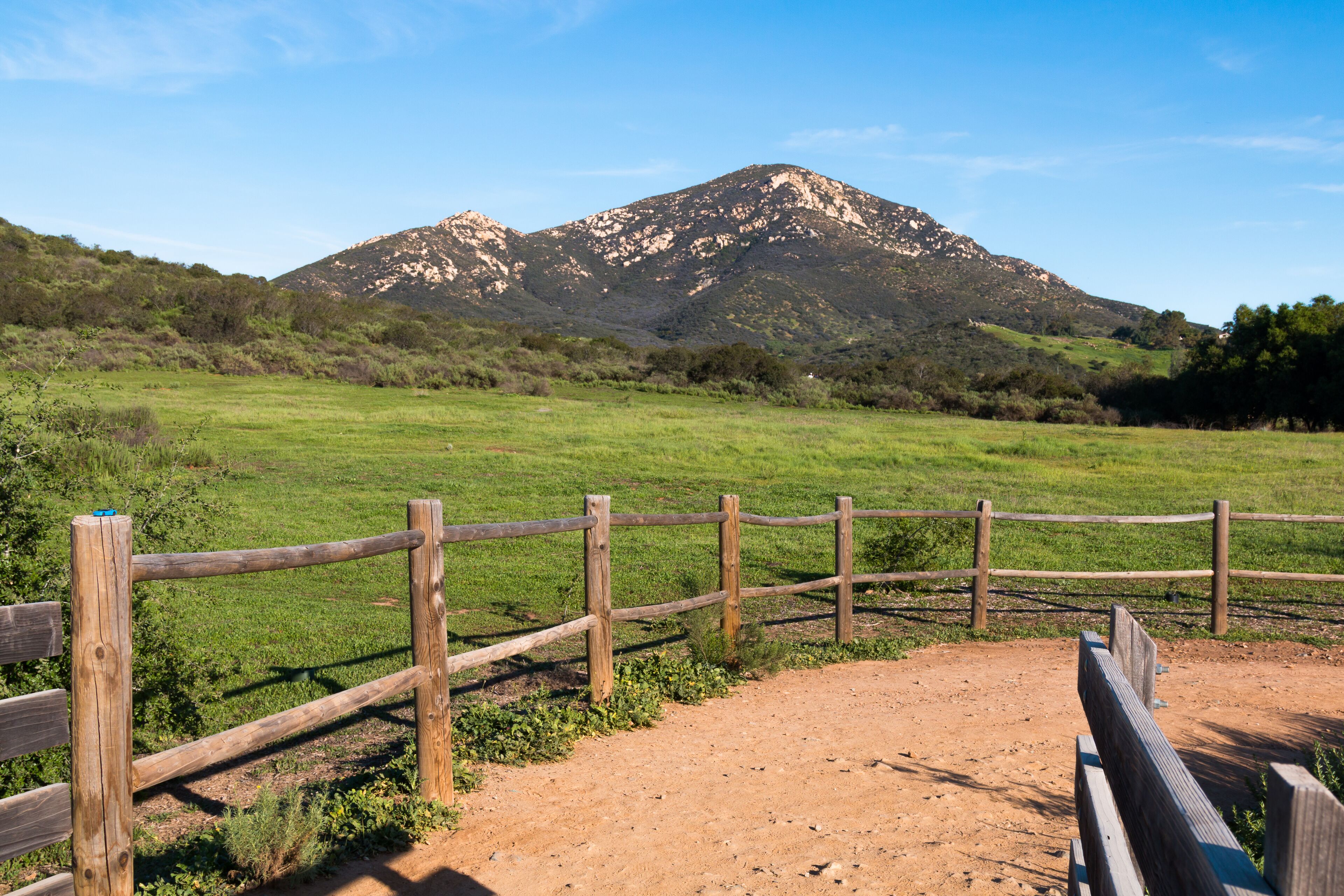 A wooden fence in a grassy field with a mountain in the background.
