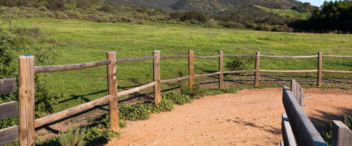A wooden fence in a grassy field with a mountain in the background.
