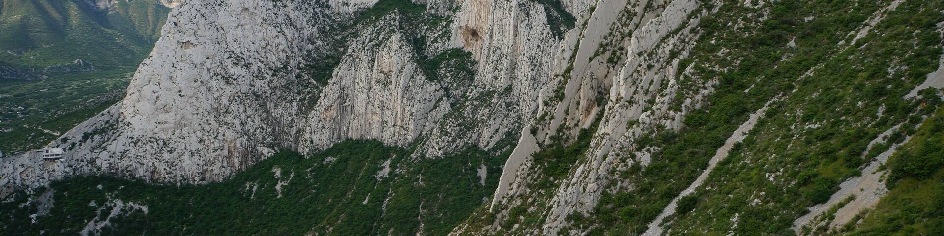 A mountainous landscape with rugged white rock formations and green vegetation.
