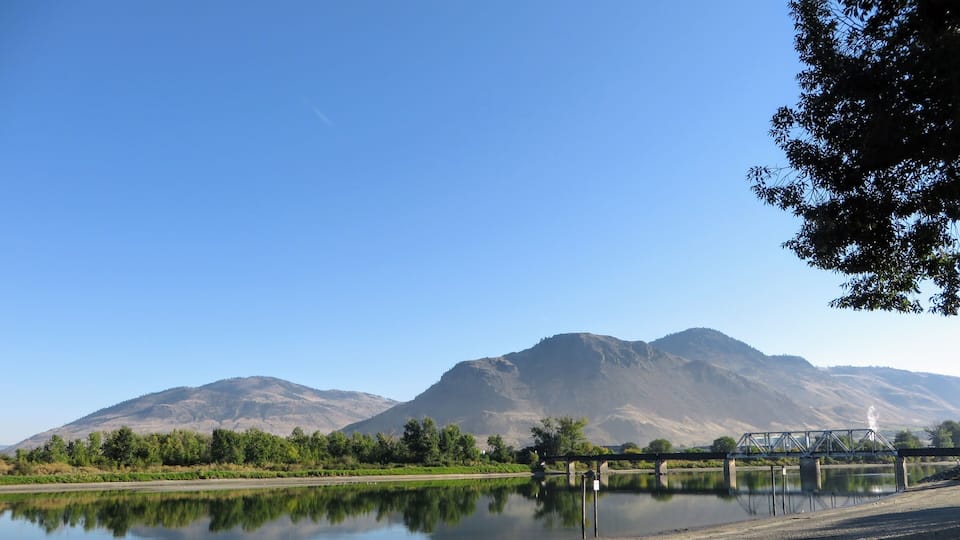 Bridge cross the North Thompson River, in Kamloops, British Columbia, Canada. Beautiful reflection of the clouds, sky, and mountain in the river.