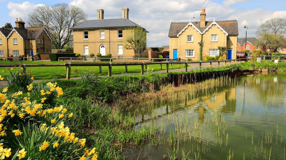A canal with a wooden bridge, houses with brick walls, and yellow daffodils in the foreground.