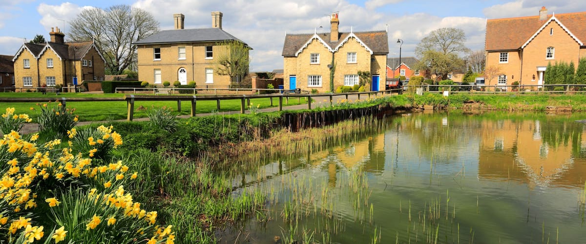 A canal with a wooden bridge, houses with brick walls, and yellow daffodils in the foreground.