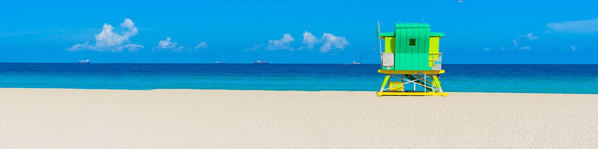 A beach with a lifeguard tower, clear blue sky, and calm ocean.