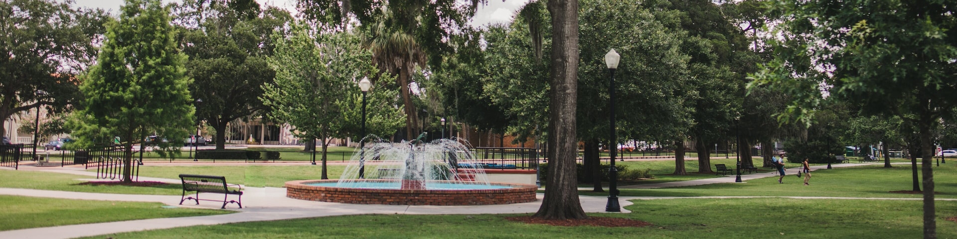 A park with a central fountain, surrounded by trees and benches.