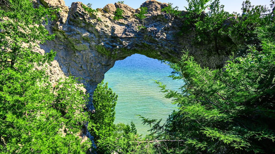 Ein natürlicher Felsbogen über einem klaren, blauen See, umgeben von dichtem Grün.