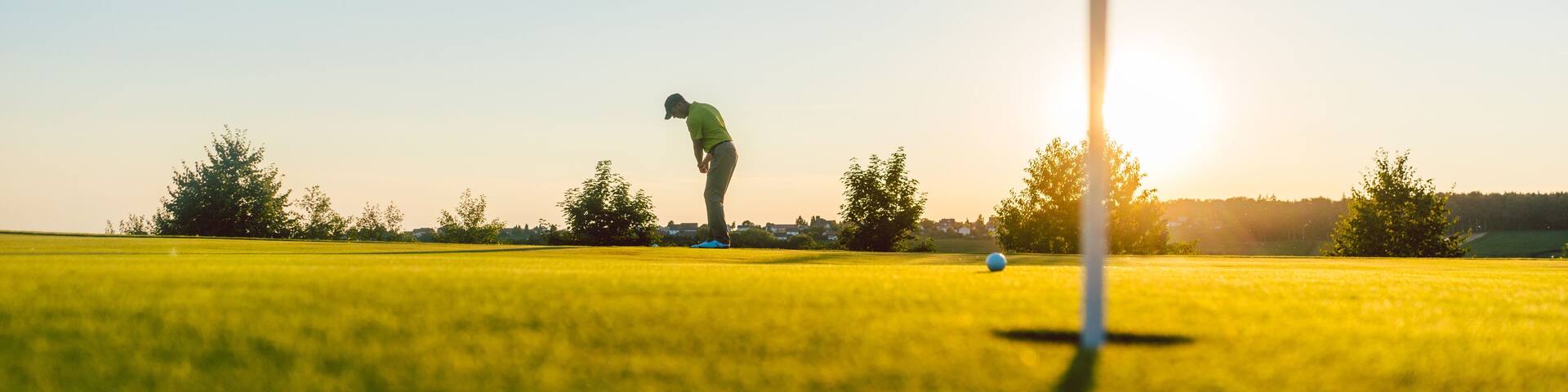 Full length view of the silhouette of a male player, hitting a long shot on the putting green of a professional golf course of a modern country club
